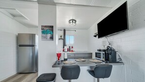 A modern kitchen with a stainless steel refrigerator, a microwave, and a flat-screen TV mounted on the wall. There are two bar stools and a small island with a sink. - Canyons Edge Route 66 Motel (Ash Fork)