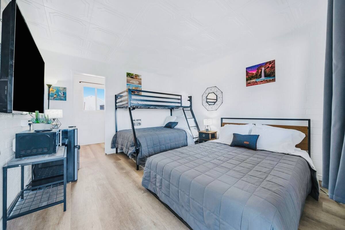 A bedroom with a bunk bed, a desk with a computer, a small table with a plant, and a nightstand with a lamp.