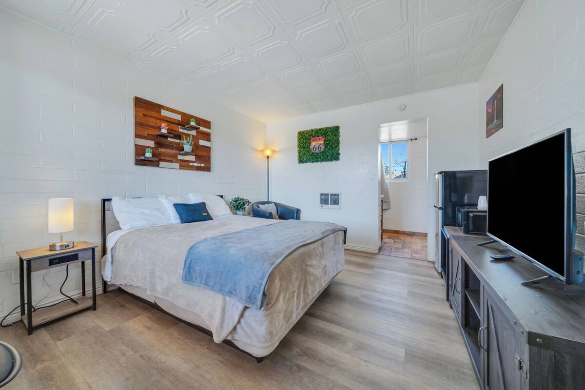 A modern bedroom with a bed, bedside table, lamp, TV, and a decorative wall piece.