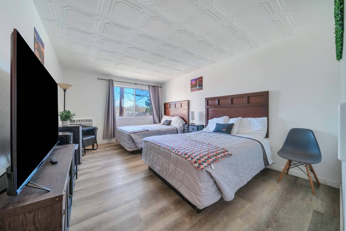 A hotel room with a large bed, a smaller bed, a desk with a computer, a TV, and a chair.