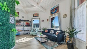 A cozy living room with a green wall, a sofa with '66' pillows, a coffee table, and a bookshelf. - Canyons Edge Route 66 Motel (Ash Fork)