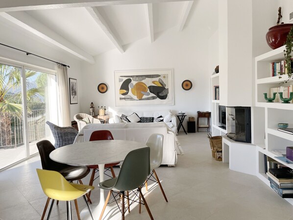 A modern living room with a dining area, white walls, and a large window.