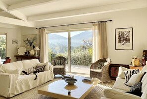 A living room with a sofa, chairs, a coffee table, and a view of mountains through large windows.