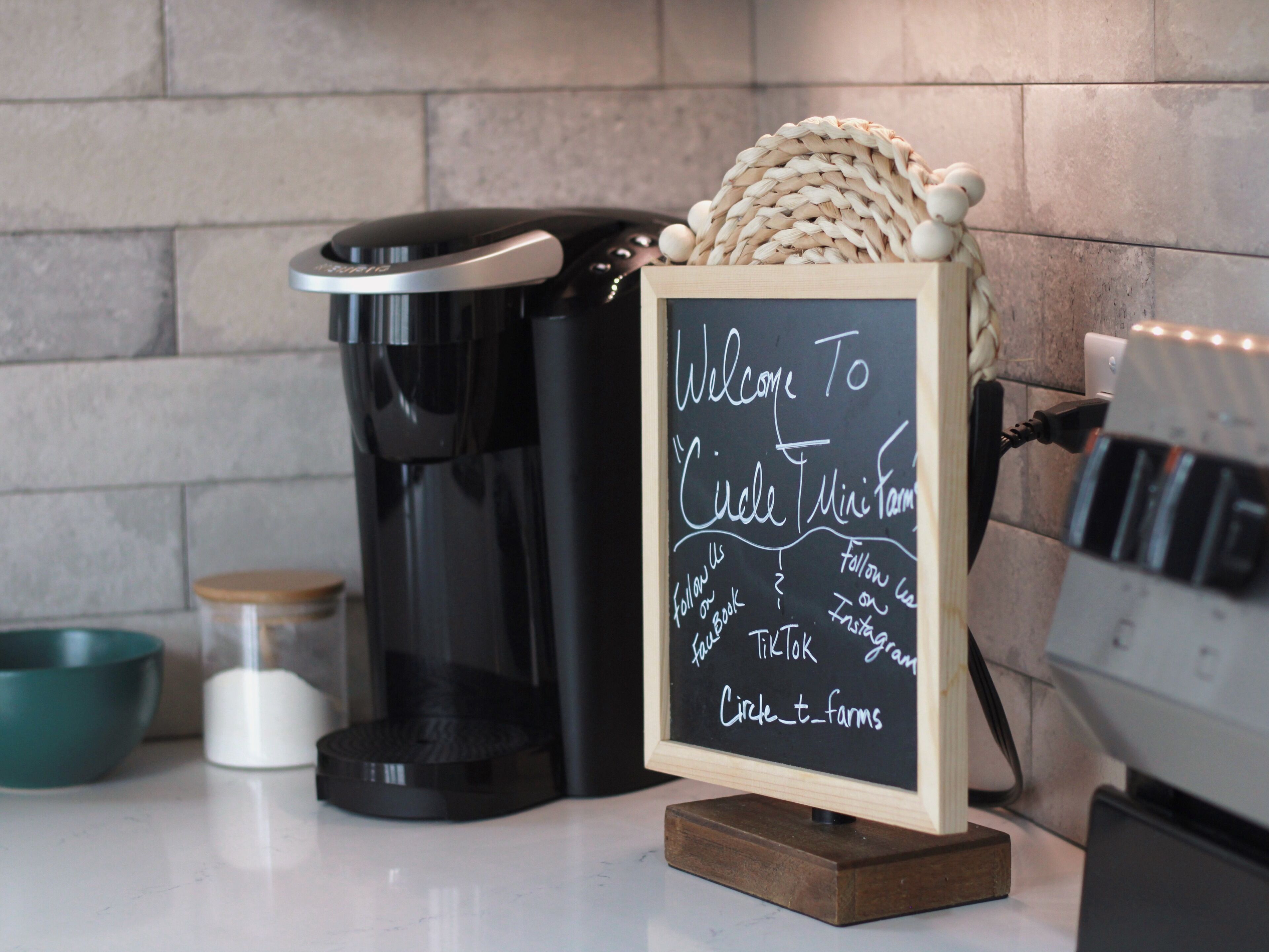 Uma máquina de café, um quadro negro e uma cesta de tecido em uma bancada.