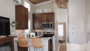 A modern kitchen with wooden cabinets, a built-in microwave, and a central island with bar stools. - Riverfront Tiny House- Fishing & Kayaking (Strawberry Plains)