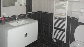 A modern bathroom with a white sink, dark tiled walls, and a white toilet.