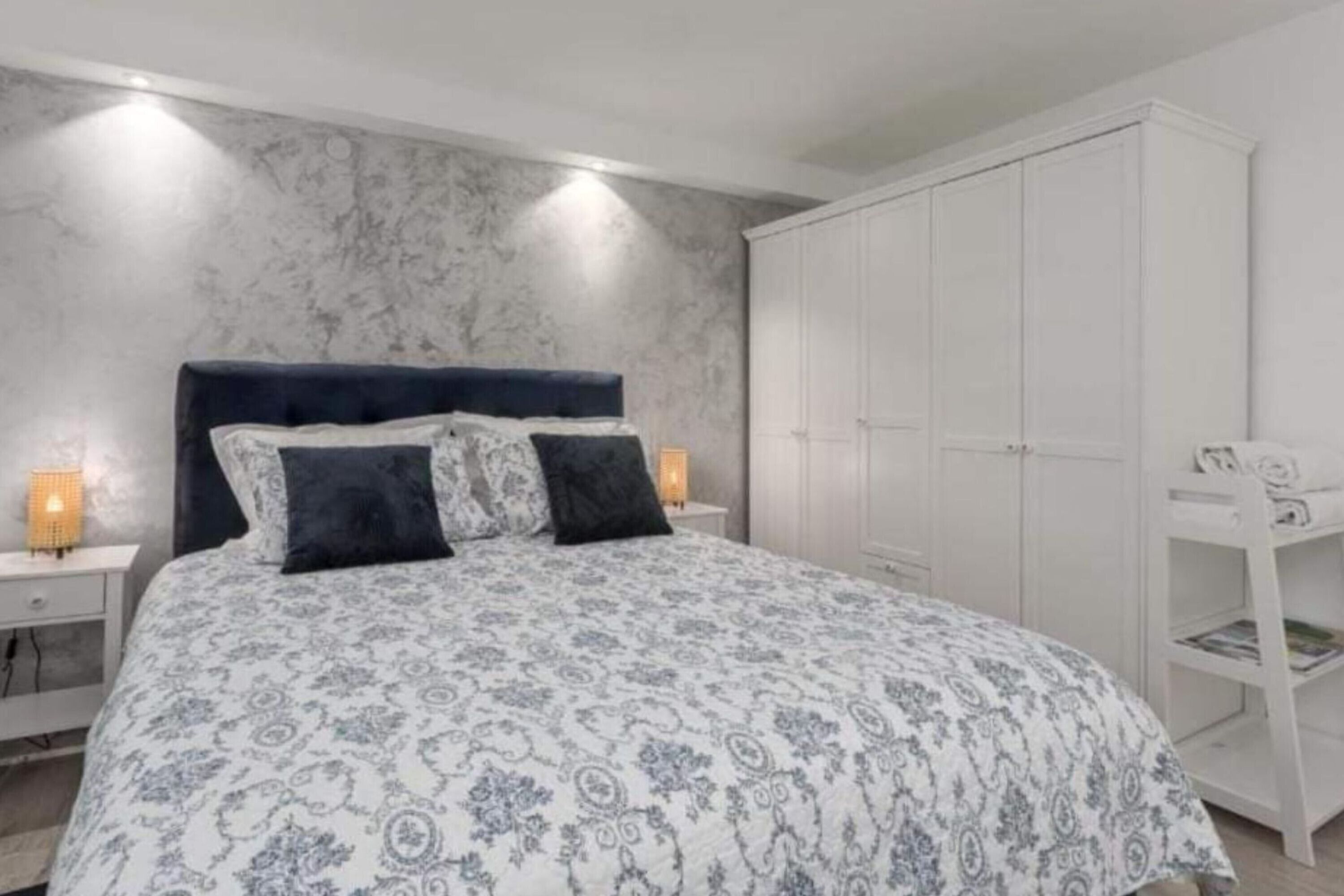 Une chambre à coucher comprenant un lit, des tables de chevet, une armoire et un bureau avec une lampe.