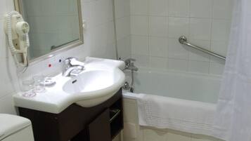A bathroom with a white sink, mirror, and toilet. There is a shower with a glass door and a white towel hanging on the wall.