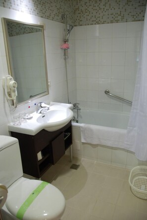 Une salle de bain avec un lavabo blanc, un miroir et des toilettes. On y trouve une douche avec une porte en verre et une serviette blanche accrochée au mur.