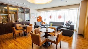A hotel lobby with wooden flooring, a bar area with glass cabinets, a seating area with sofas and chairs, and large windows with sheer curtains. - Hong Cheng Sing Business Hotel (Tainan)