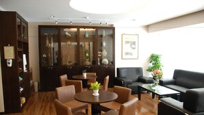 Um hall de hotel com piso de madeira, um balcão de recepção, uma área de estar com cadeiras e sofás, e um armário grande com portas de vidro.