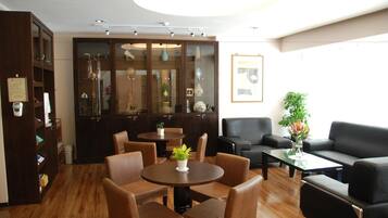 A hotel lobby with a wooden floor, a reception desk, a seating area with chairs and sofas, and a large cabinet with glass doors.