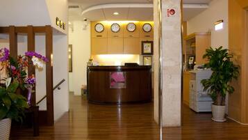 A reception area with a wooden reception desk, a clock on the wall, and a plant in the corner.