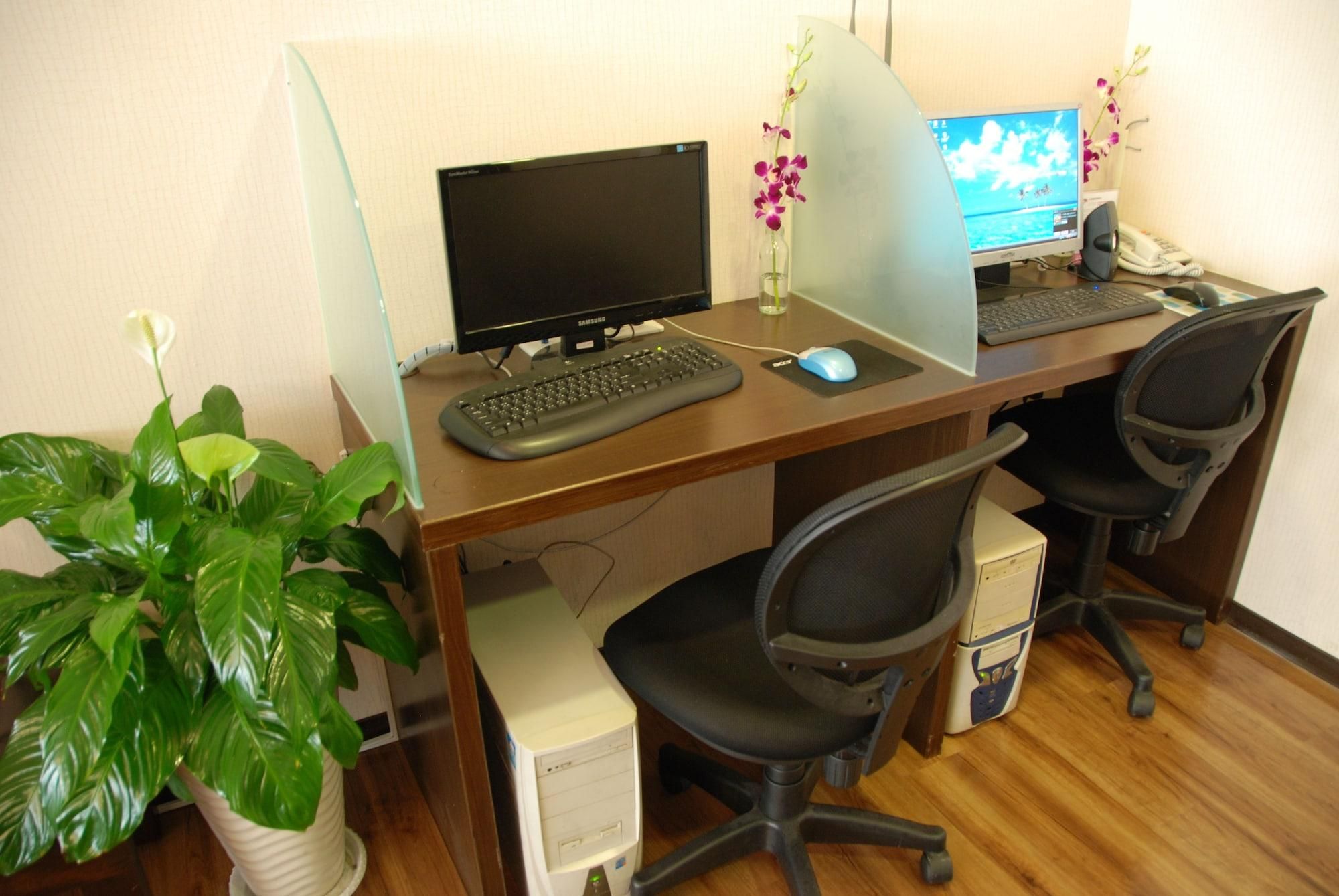 Een houten bureau met twee beeldschermen, een toetsenbord, een muis en twee bureaustoelen. Een potplant staat aan de linkerkant van het bureau.