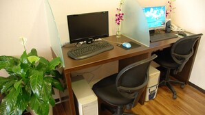 Uma secretária de madeira com dois monitores de computador, um teclado, um rato e duas cadeiras de escritório. Há uma planta em vaso no lado esquerdo da secretária.