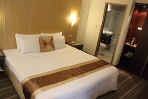 Habitación de hotel con una cama grande, una mesita de noche, un tocador, un espejo y vistas al baño.
