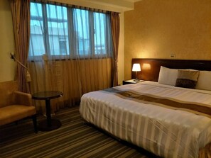 A hotel room with a large bed, a small round table, a chair, and a window with curtains.