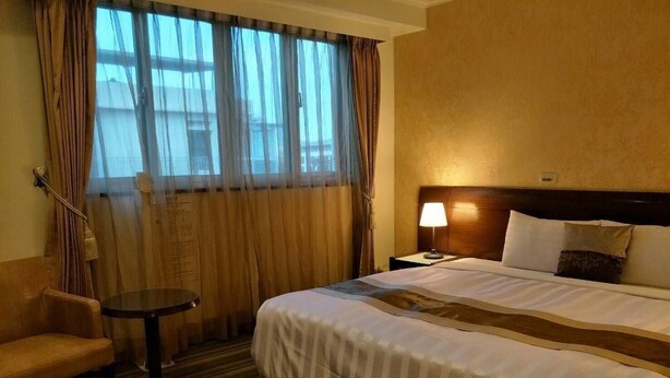 A hotel room with a large bed, a small round table, a chair, and a window with curtains. - Hong Cheng Sing Business Hotel (Tainan)
