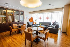 A hotel lobby with wooden flooring, a bar area with glass cabinets, a seating area with sofas and chairs, and large windows with sheer curtains. - Hong Cheng Sing Business Hotel (Tainan)