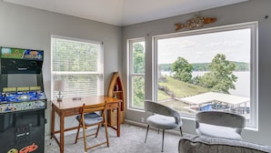 A room with a large window, a wooden table, two chairs, and a classic arcade game. - Views & Private Dock: Lake of the Ozarks Retreat! (Climax Springs)