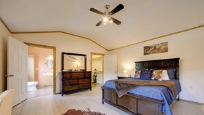 Un dormitorio con una cama, un ventilador de techo, un aparador de madera y una alfombra de cuero de vaca.