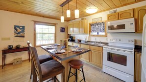 Una cocina con armarios de madera, un microondas, un horno y un comedor con mesa y sillas.