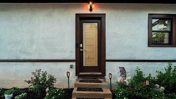 A house with a brown door, a window with blinds, and a small garden with flowers and a stepping stone pathway.