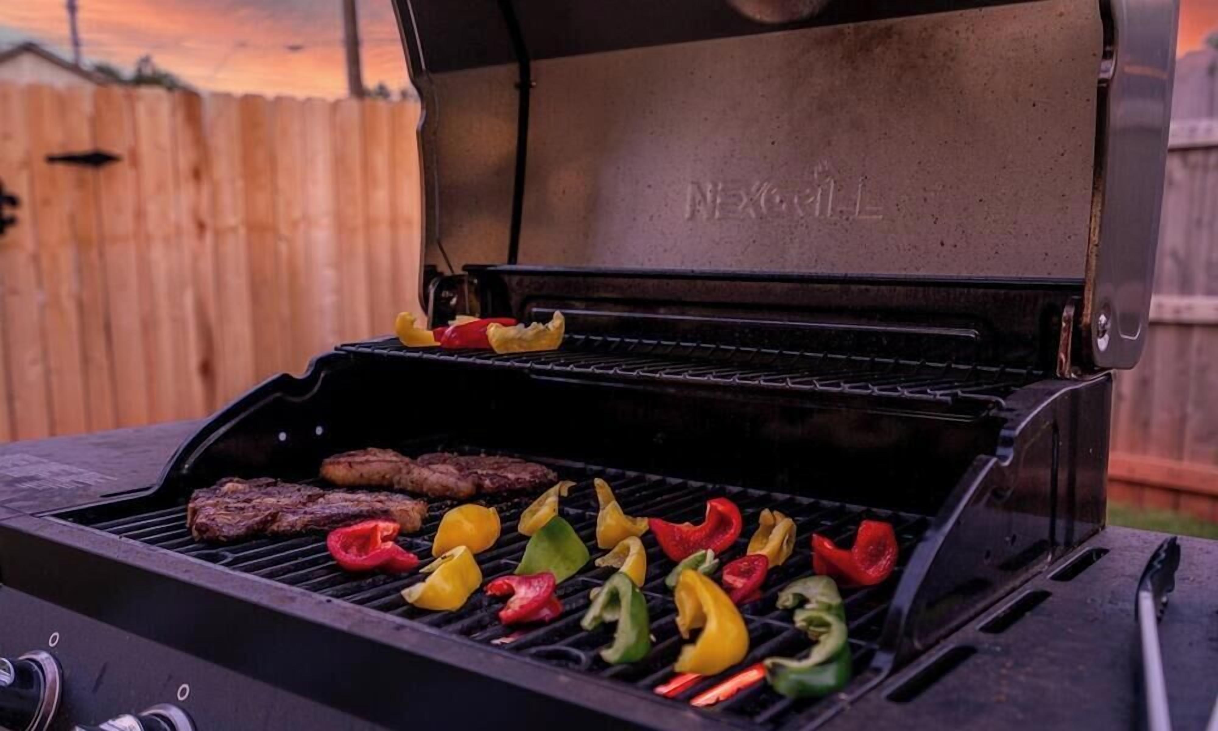 Una parrilla con varios alimentos cocinándose, incluyendo filetes y pimientos.