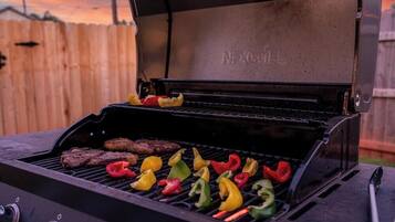 Una parrilla con varios alimentos cocinándose, incluyendo filetes y pimientos.