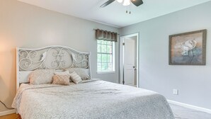 Un dormitorio con cama, ventilador de techo, ventana con cortinas y puerta.