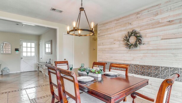 Un comedor con una mesa y sillas de madera, una araña y un adorno decorativo en la pared.