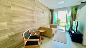 A modern living room with a sofa, a wooden chair, a small table, and a TV stand. - Cond. Azul Mar Porto de Galinhas (Ipojuca)