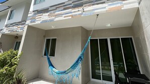 A multi-story residential building with a balcony, a hammock, and a patio area with a table and chairs. - Cond. Azul Mar Porto de Galinhas (Ipojuca)