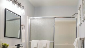 A bathroom with a white vanity, a large mirror, a shower with frosted glass doors, and a marble floor. - Peaceful Woodland Apt C_Acadia National Park (Seal Cove)