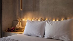 A bed with white linens, a bedside table with a basket and flowers, and a wall with a textured pattern and a vertical light fixture.