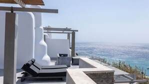 A modern outdoor lounge area with a view of the sea, featuring concrete seating and a pergola structure.