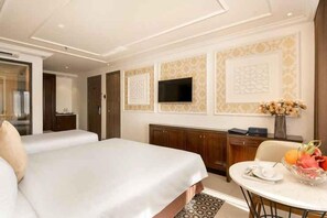 A hotel room with two beds, a dining table with fruit, a TV, and a decorative wall panel. - Bella Merry Hotel and Apartment (Da Nang Municipality)