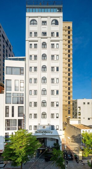 Een hotel met meerdere verdiepingen, ontworpen in een klassieke stijl, met een centrale ingang met een bordje, en omringd door andere gebouwen.