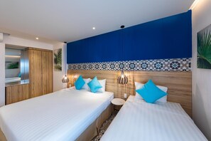 Quarto de hotel com duas camas, um guarda-roupa de madeira, uma mesinha redonda e um painel decorativo na parede.