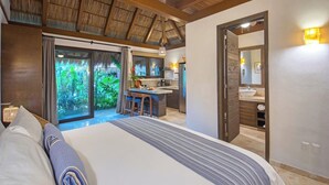 A bedroom with a large bed, a view of the garden through the window, a kitchen area, and a bathroom with a mirror. - Villa Tayrona (Bucerías)
