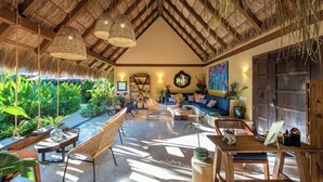 A spacious room with a thatched roof, a sofa set, a dining table, and a variety of plants. - Villa Tayrona (Bucerías)