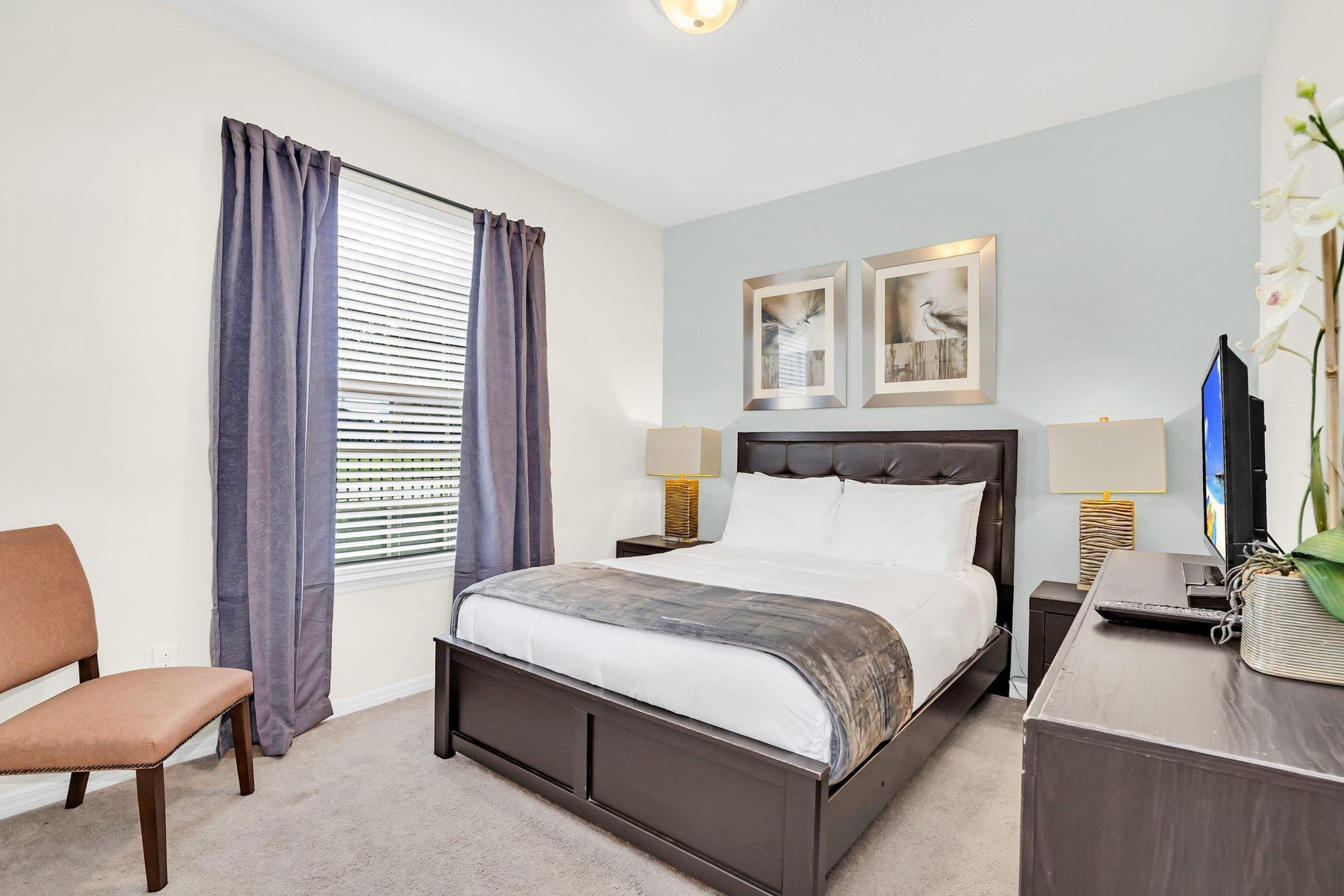 A bedroom with a bed, two bedside tables, a desk, a chair, and a window with curtains.