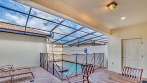 Un patio exterior con piscina, asientos cubiertos y una puerta.