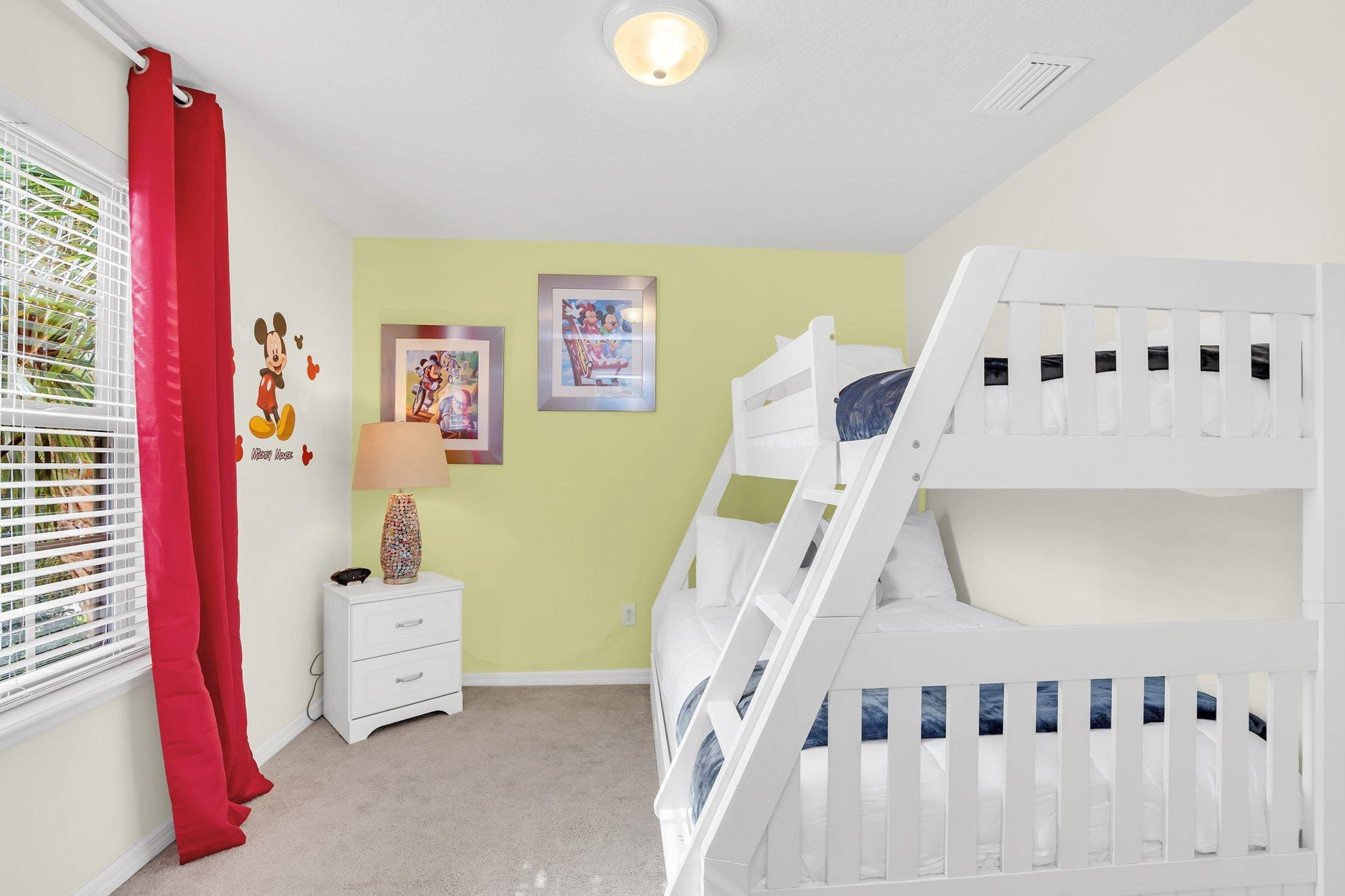 A child's room with a bunk bed, a nightstand, a lamp, and wall decorations.