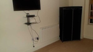 Ein Zimmer mit einem an der Wand befestigten Flachbildfernseher, einem Heizkörper und einem schwarzen Kleiderschrank.