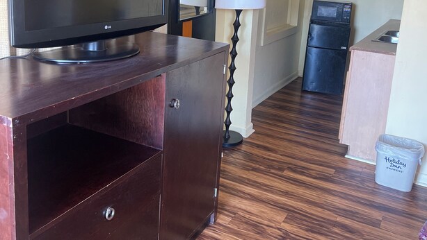 A hotel room with a wooden entertainment center, a flat-screen TV, a lamp, a microwave, and a trash bin. - Economy Inn San Marco (Jacksonville)