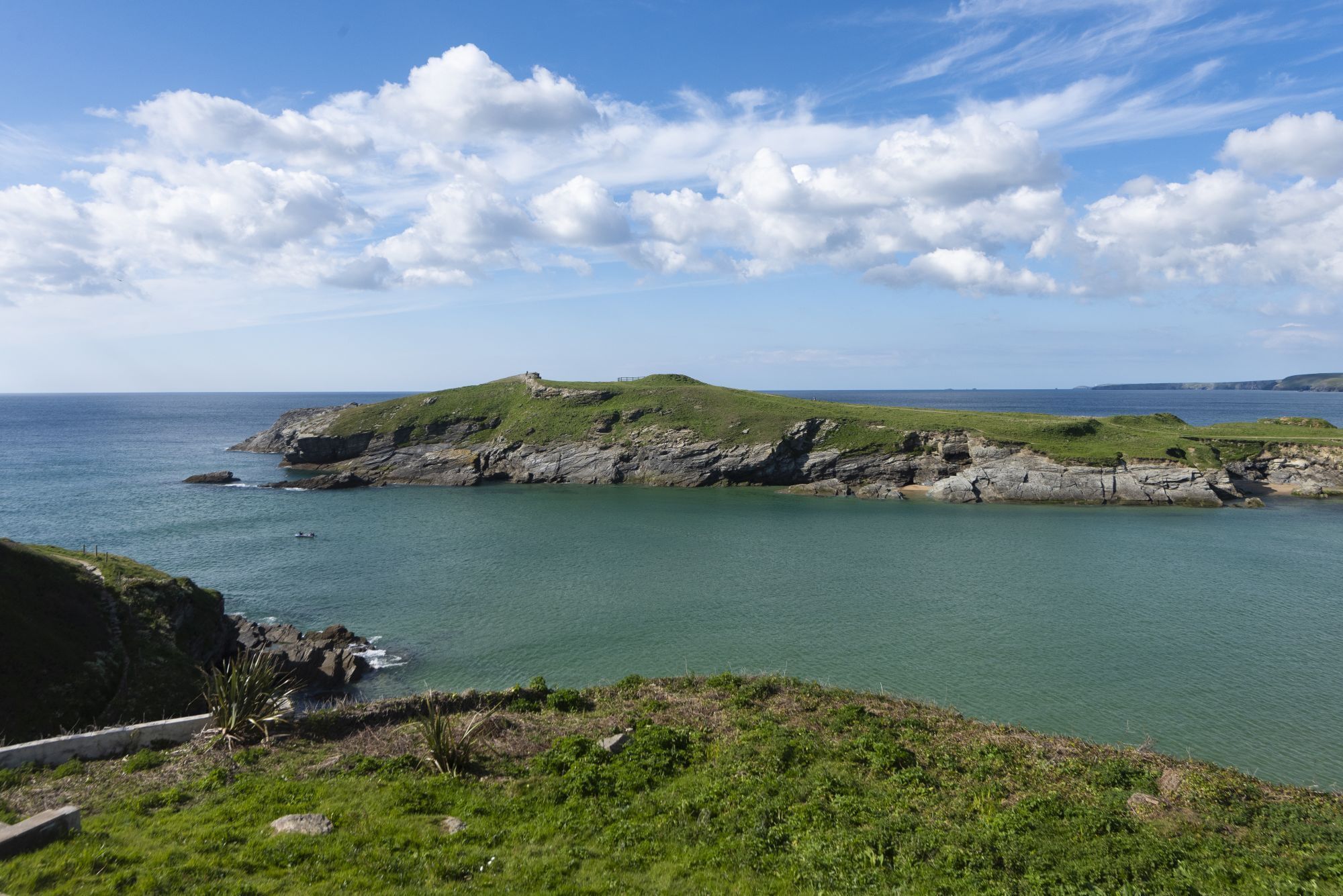 A coastal landscape with rocky cliffs, grassy areas, and a clear view of the sea.