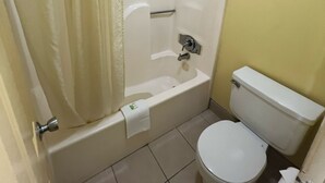 A small bathroom with a bathtub, toilet, and shower curtain. - Antler's Inn (Cuero)