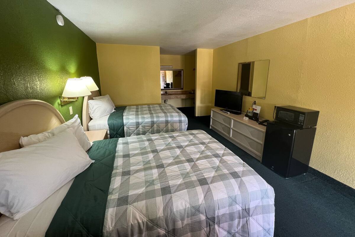 A hotel room with two beds, a dresser, a television, and a microwave.