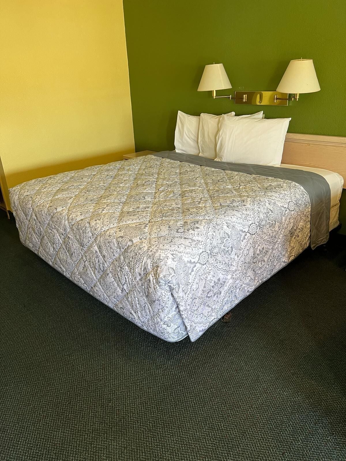 A hotel room with a large bed, two bedside lamps, and a green accent wall.